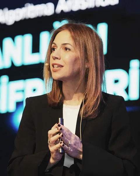 Defne İncekara, TEDxOSTİMTech sahnesinde konuşurken; siyah ceket, elinde sunum kumandası.